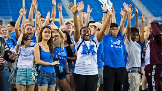 Group of smiling students raising their hands up on Kroger Field